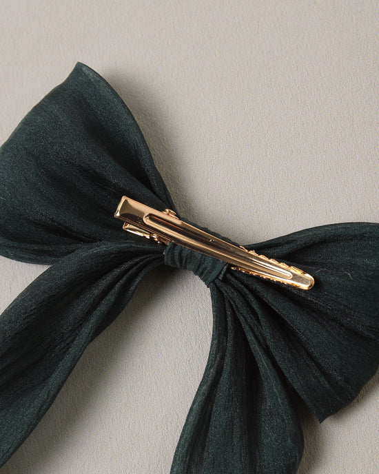 A dark forest green fabric hair bow with a gold metal hair clip, shown against a neutral light gray background.