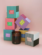 Collection of colorful candle boxes with a single candle on a pink background