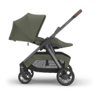 A stroller in olive green fabric with a dark gray frame and brown handle grips, shown from the side against a plain white background.