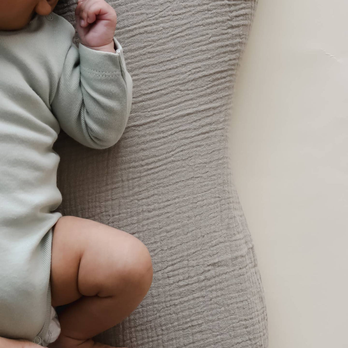 Child sitting on a textured surface wearing a light-colored outfit