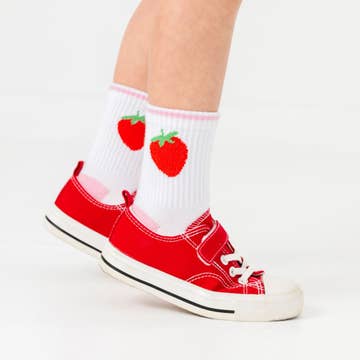 Red sneakers with white soles worn with socks featuring red strawberry designs on a light gray background
