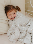 Child wrapped in a white blanket, smiling, on a light-colored couch.