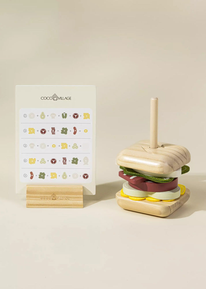 Wooden toy hamburger with a straw next to a stand with illustrations on a beige background