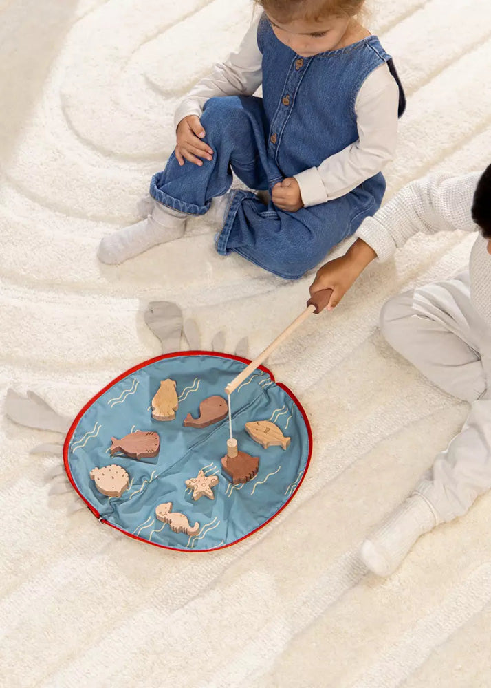 Child playing with a fishing game on a blue mat with sea creature figures, sitting on a white blanket.