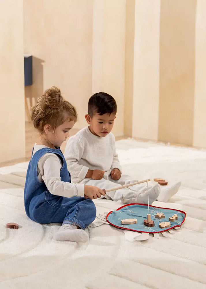 Two children playing with wooden toys on a bed.