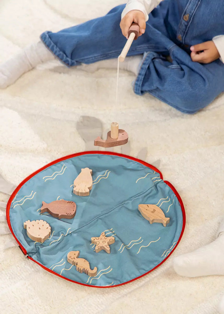 Child playing with wooden toys on a blue mat with sea creature designs.