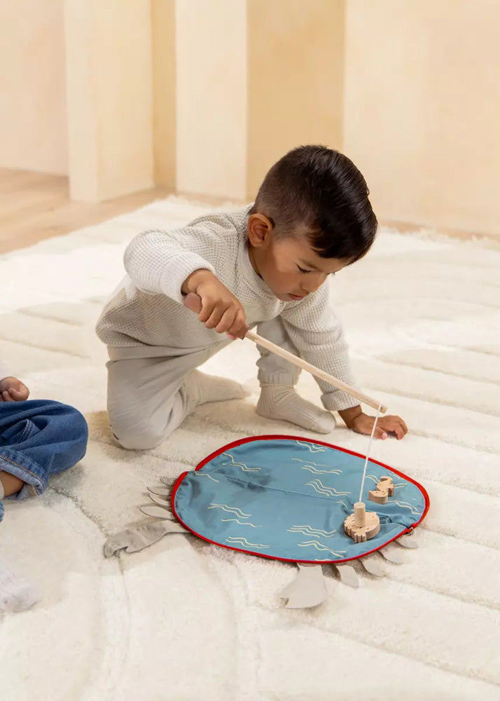 Child playing with a wooden toy on a blue mat in a room.