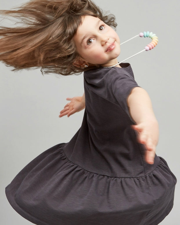 A young girls wearing gray dresses standing against a plain background