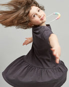 A young girls wearing gray dresses standing against a plain background