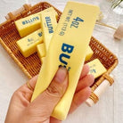 Hand holding a stick of butter with a wicker basket in the background
