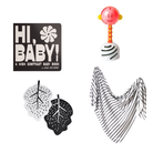 A baby gift set featuring a black book titled 'HI, BABY! A HIGH CONTRAST BABY BOOK' with white lettering, a pink and orange baby rattle, two black and white leaf-shaped items, and a black and white striped triangular scarf, all arranged on a plain white background.