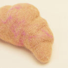 Felted cloud-shaped object with pink speckles on a beige background