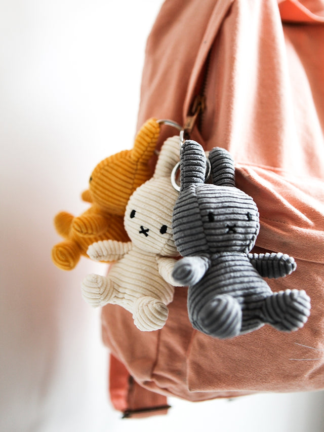 Two plush keychains, one gray and one beige, hanging from a pink bag.