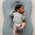 Baby lying on a gray cushion with a neutral background
