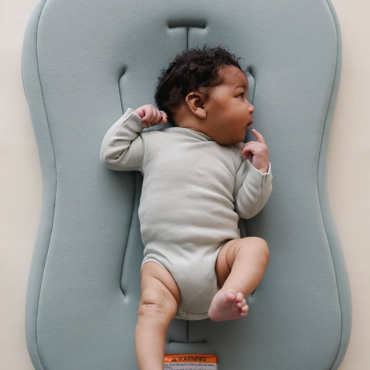 Baby lying on a gray cushion with a neutral background