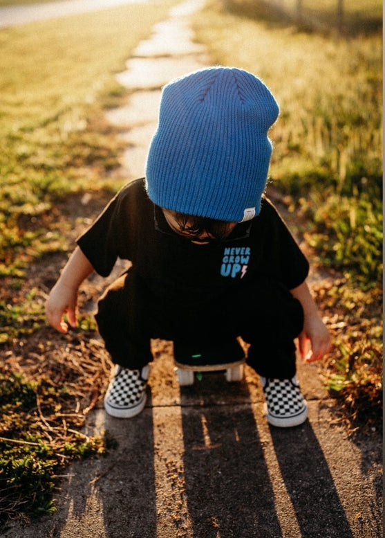 Child wearing a blue beanie and black shirt with text, standing on a skateboard outdoors.