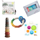 A collage of four baby toys on a white background: a white fabric safari-themed teething bag with animal illustrations, a boxed set of soft building blocks, a rainbow-colored ring teether with blue rings, and a boxed set of colorful sensory balls labeled dimPL.