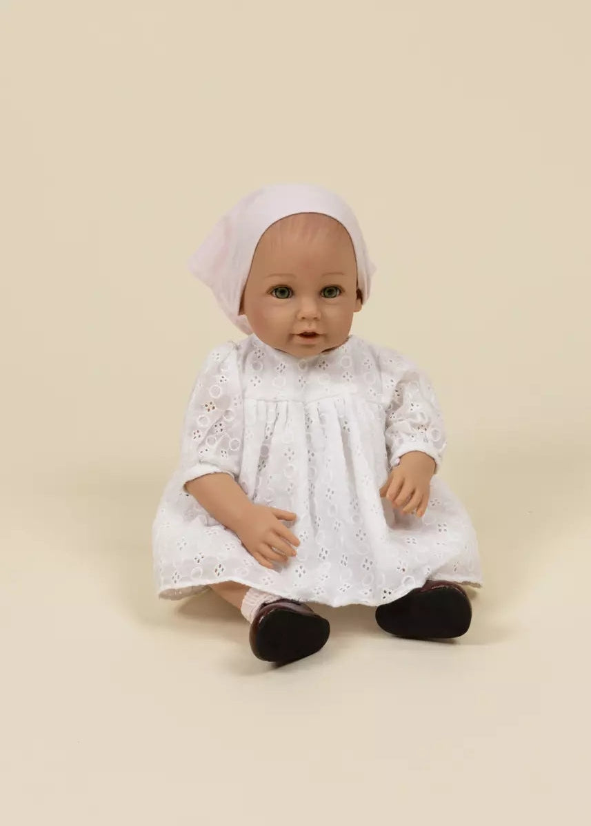 Doll wearing a white lace dress and headscarf on a beige background
