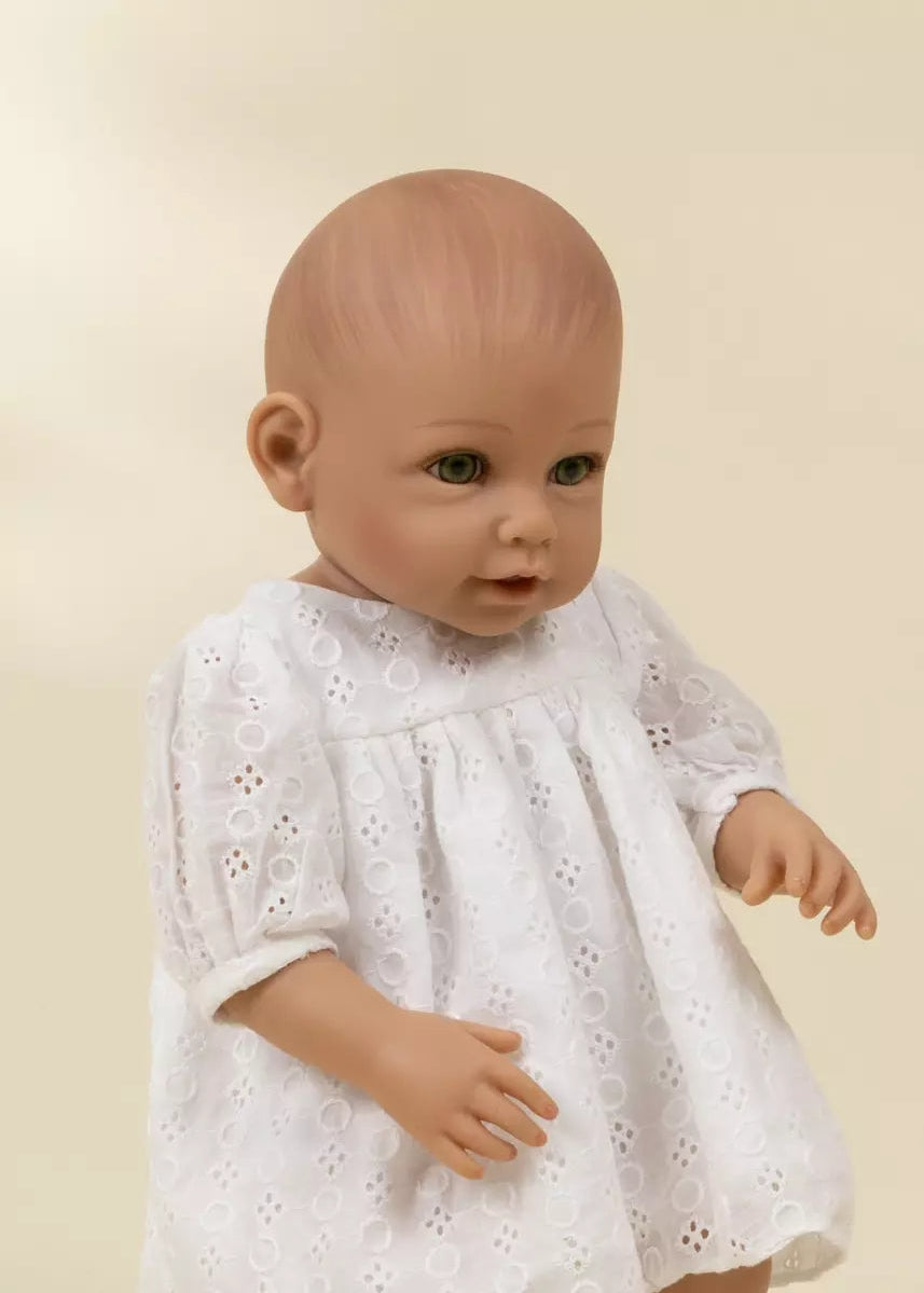 Baby doll wearing a white dress against a beige background