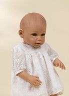 Baby doll wearing a white dress against a beige background