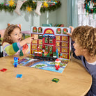 Two children playing with a toy set on a table, surrounded by Christmas decorations.