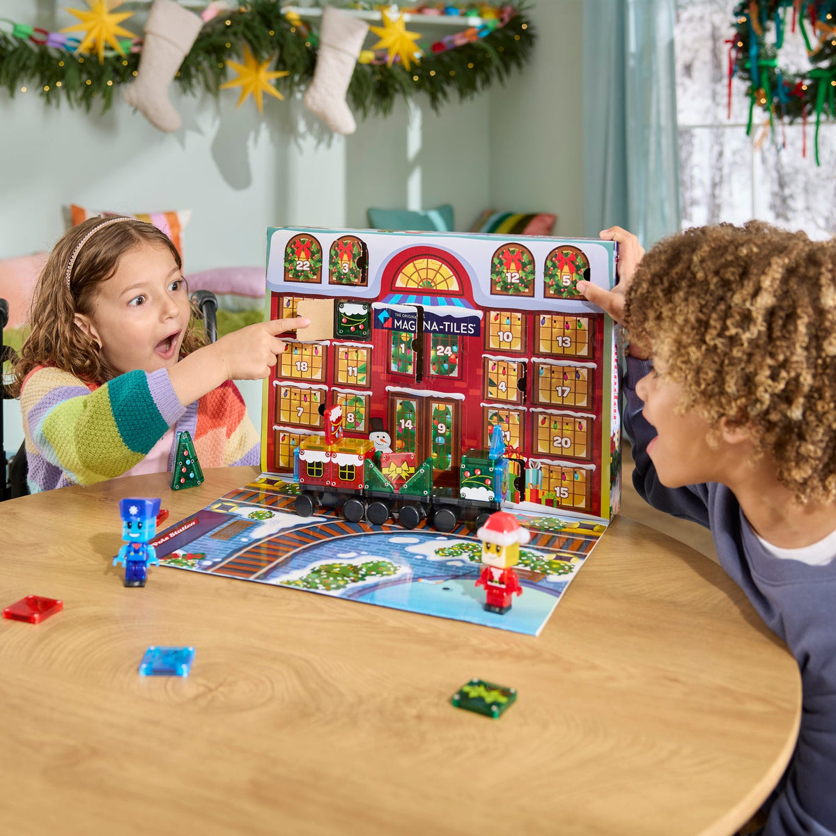 Two children playing with a toy set on a table, surrounded by Christmas decorations.