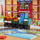 A colorful wooden toy train set with a blue robot passenger on a holiday advent calendar track, with a red advent calendar box in the background.