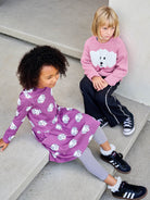 Two children sitting on a concrete step wearing matching outfits with bear patterns.