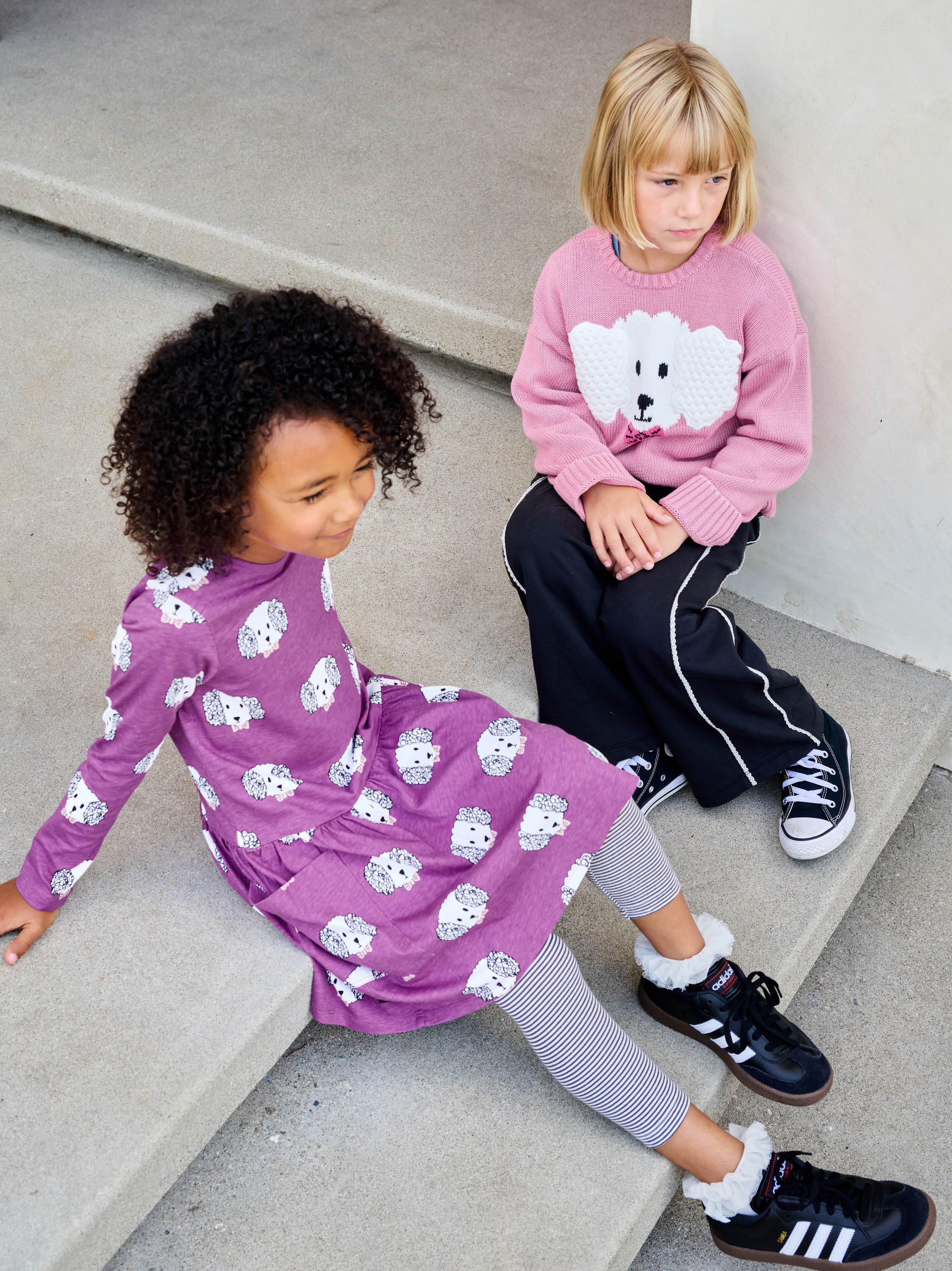 Two children sitting on a concrete step wearing matching outfits with bear patterns.