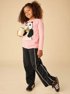Child wearing a pink shirt with a panda design and black pants, holding a drink.