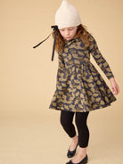 Young girl wearing a patterned dress with long sleeves and a white knit hat on a beige background