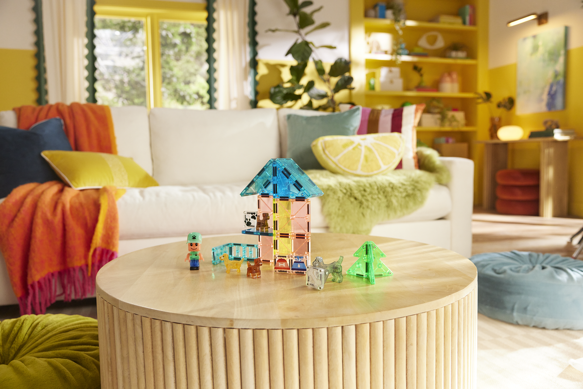 Children's playroom with colorful toys on a wooden coffee table, white sofa with cushions, and yellow walls.