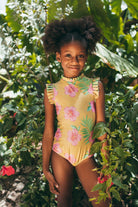 Young girl in a floral swimsuit standing among green foliage