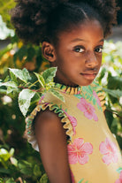 Young girl in a floral dress standing among green foliage