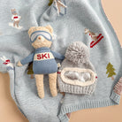 Teddy bear in ski outfit with goggles and a matching hat on a knitted blanket with winter patterns.