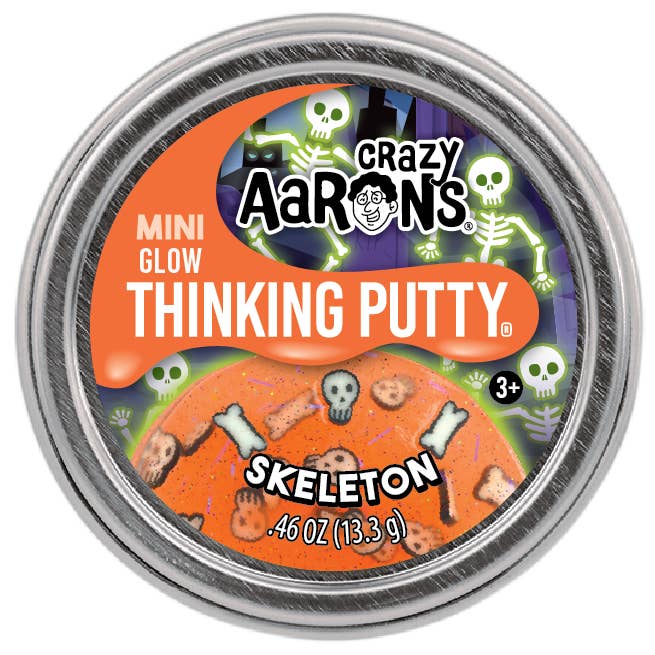 A round metal tin of Crazy Aaron's Mini Glow Thinking Putty in the Skeleton flavor, featuring an orange and purple label with cartoon skeletons and bones.