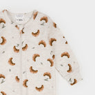 A long-sleeve baby romper by Firsts for Children, featuring an all-over print of brown croissants and small green sprigs on a light cream heathered fabric, with a front zipper.