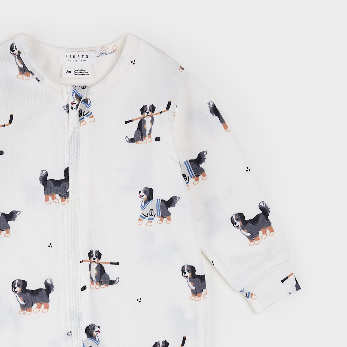 A long-sleeve baby zip-up sleeper by First75, featuring an all-over print of Bernese Mountain Dog puppies wearing hockey gear on a white background.