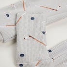 Close-up a light gray ribbed fabric, featuring an all-over print of hockey pucks and sticks in brown, white, and navy blue on a white backgroud.