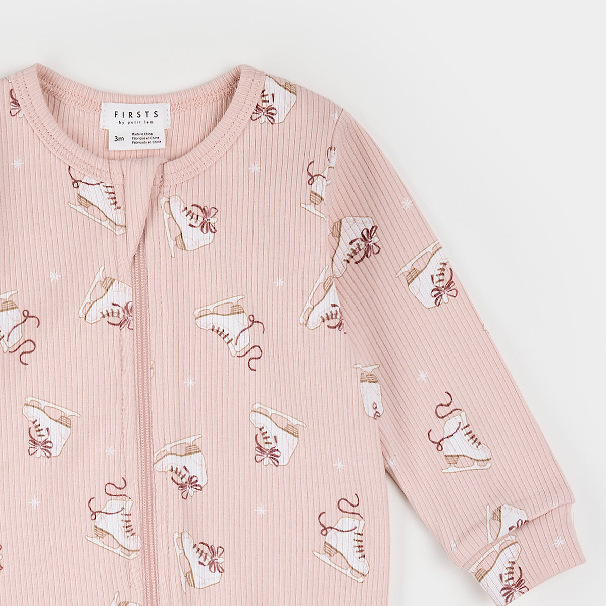 A pink long-sleeve baby cardigan with a front zipper, featuring an all-over print of white and brown ice skates with small white star details, shown on a clean white background.