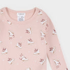 A close-up of a children's long-sleeve top in light pink waffle fabric, featuring an all-over print of white ice skates with brown laces and small white star accents. The brand label 'FIRSTS FOR KITTEN' is visible inside the collar.