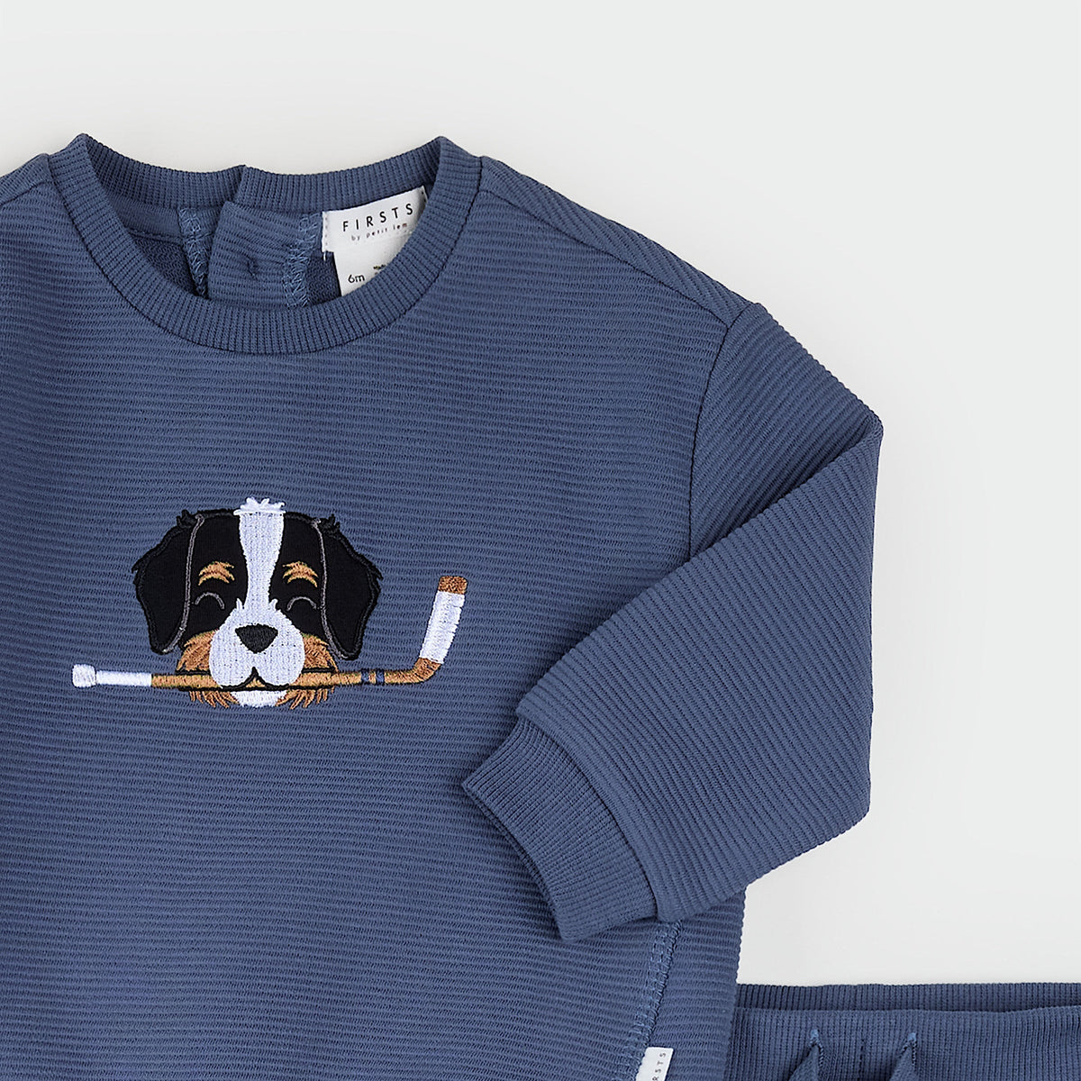 A navy blue ribbed long-sleeve children's sweatshirt with an embroidered dog graphic holding a hockey stick on the chest, shown on a light gray background.