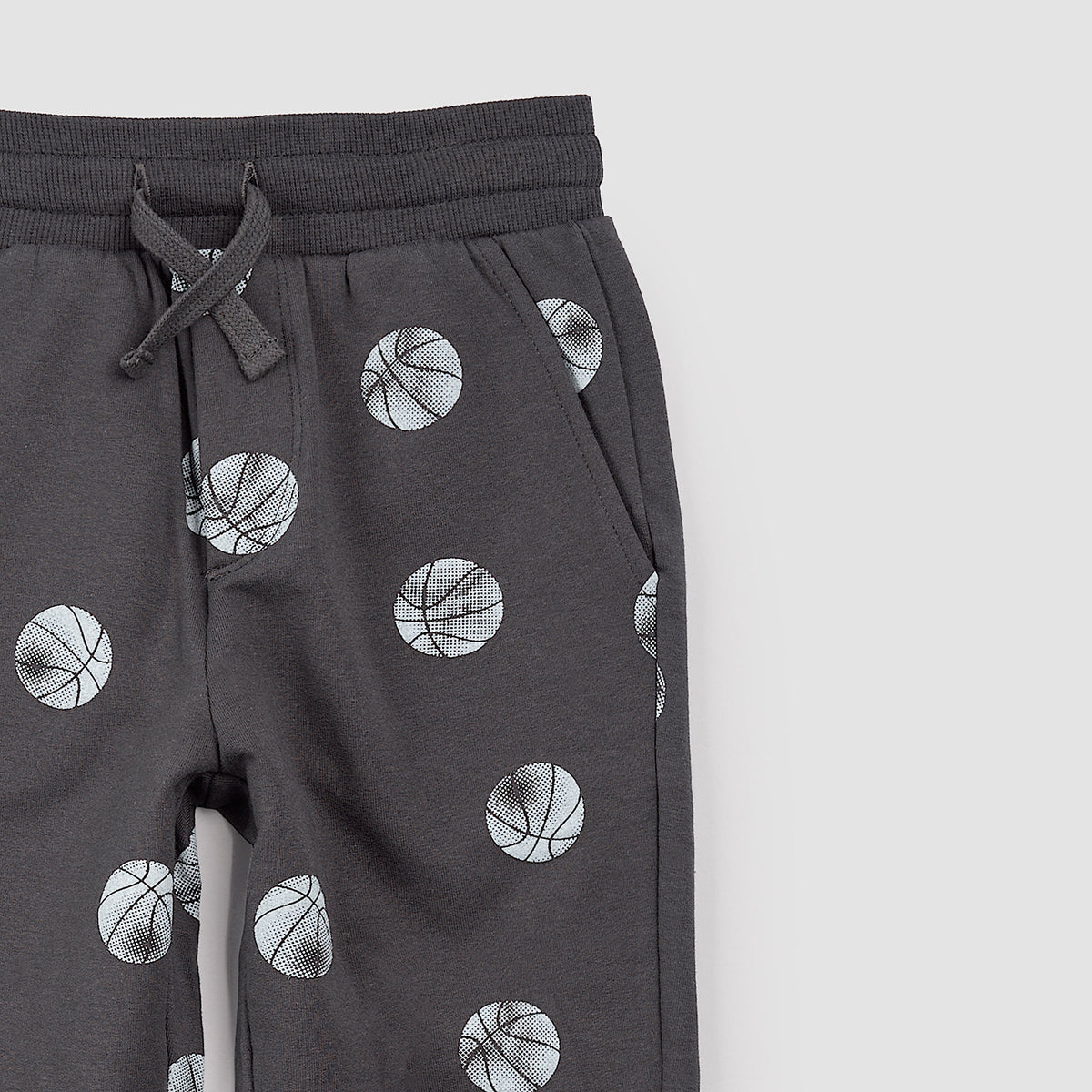 Close-up dark gray jogger pants with an all-over basketball print, featuring a drawstring waist and ribbed cuffs, shown against a plain white background.