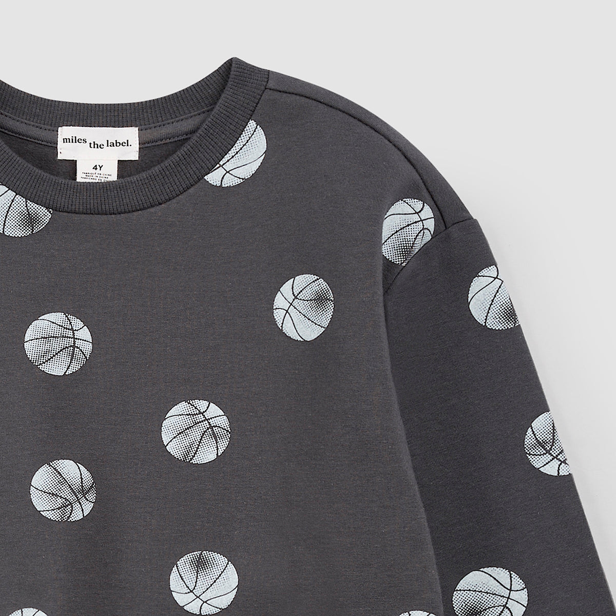 Close-up a dark gray crewneck sweatshirt with an all-over print of basketballs in white and light gray, shown flat against a solid white background.