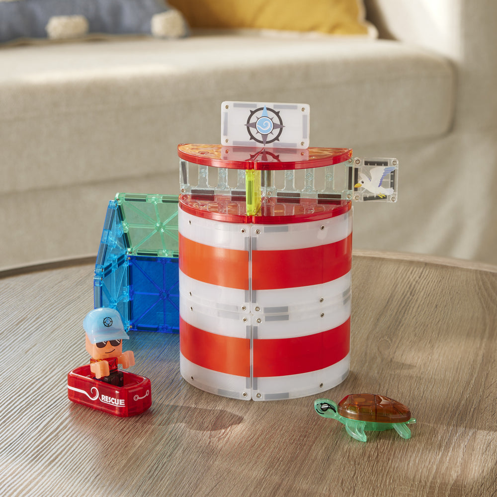 The Magna-Tiles Lighthouse Rescue set built on a wooden coffee table, featuring a red-and-white striped cylindrical lighthouse structure, a rescue raft with a character figurine, and a sea turtle figure.