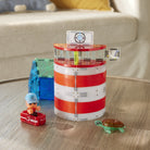 The Magna-Tiles Lighthouse Rescue set built on a wooden coffee table, featuring a red-and-white striped cylindrical lighthouse structure, a rescue raft with a character figurine, and a sea turtle figure.