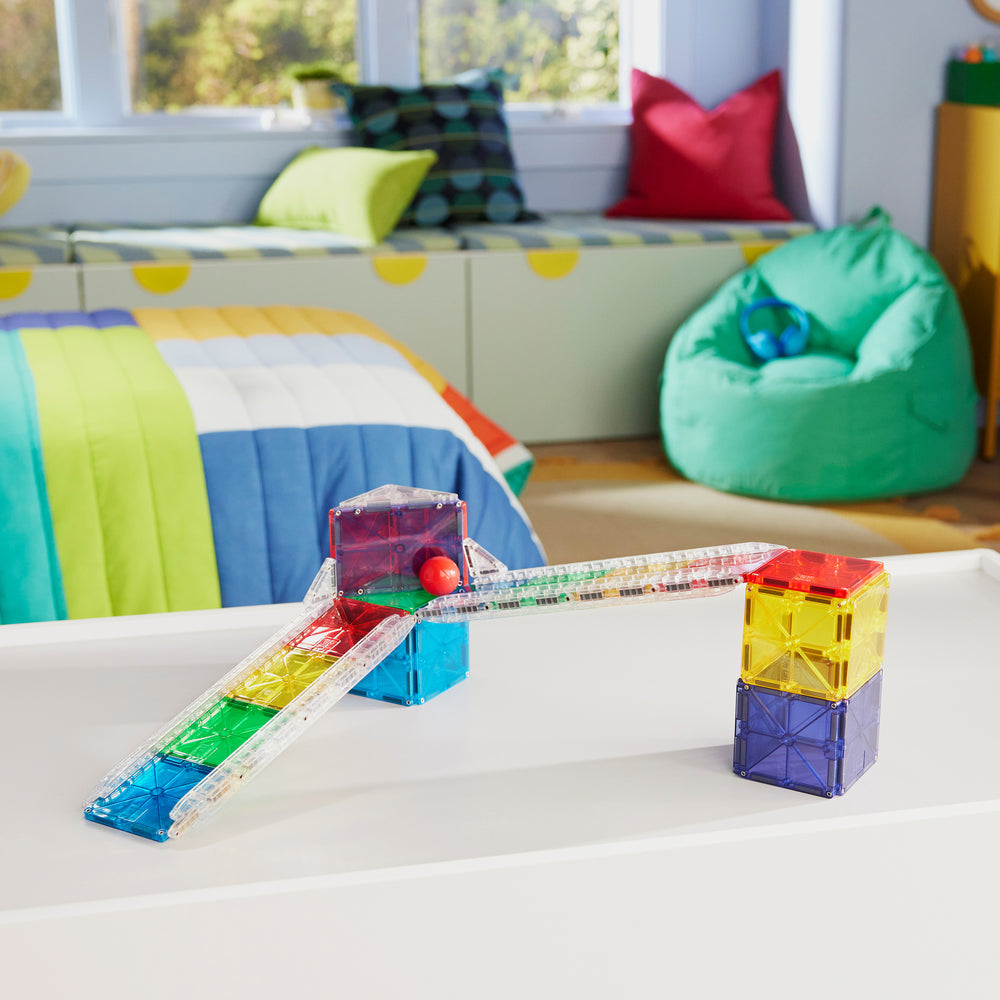 A custom track structure built with colorful magnetic tiles and clear rail pieces from the Magna-Tiles Rail Racers set, featuring a rolling ball on an elevated ramp.