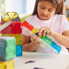 A child builds a custom track structure using colorful magnetic tiles and a clear rail piece from the Magna-Tiles Rail Racers set.