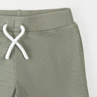 Green ribbed pants with white drawstring on a light gray background