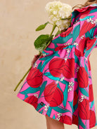 Ruffle Shoulder Ballet Dress - Tulip Twist in Pink by Tea Collection featuring long sleeves, a crew neckline, ruffled shoulder details, and an artist-drawn red and teal tulip floral pattern over a pink background, viewed from the side while holding a large white flower.